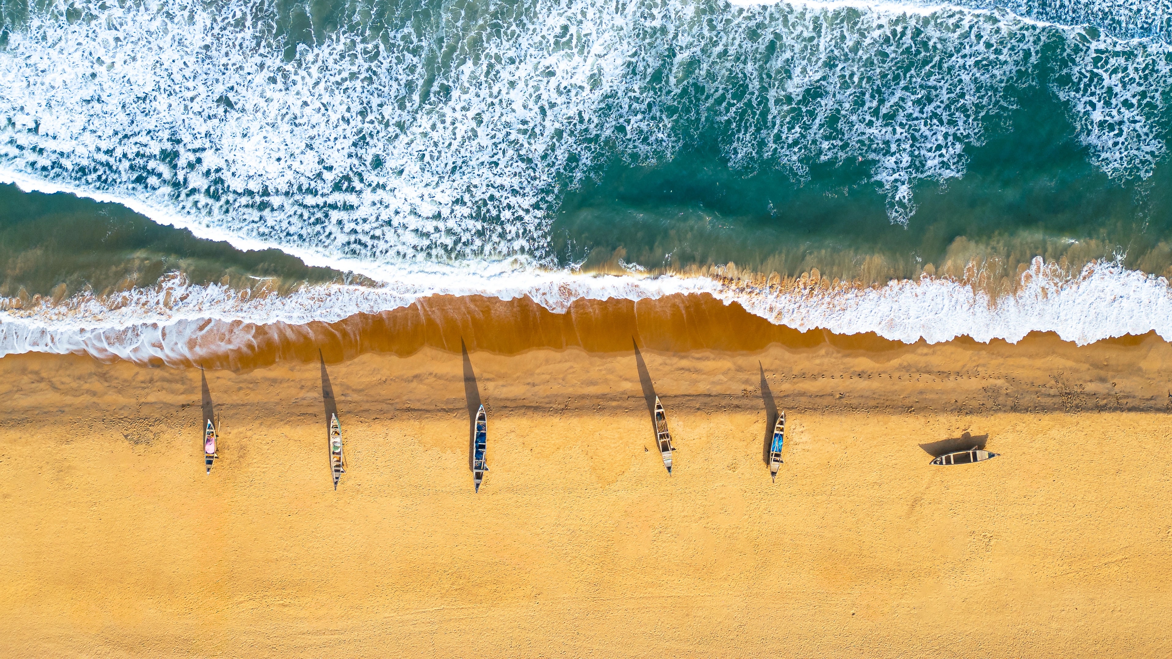 An aerial view of people beside waves meeting a golden beach in Ghana