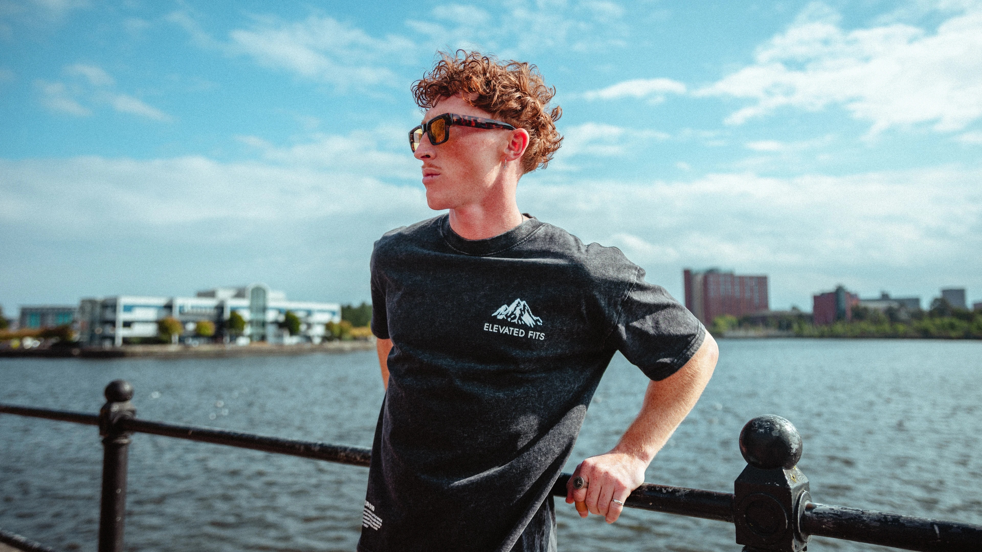 A streetwear portrait beside the water beneath a blue UK sky