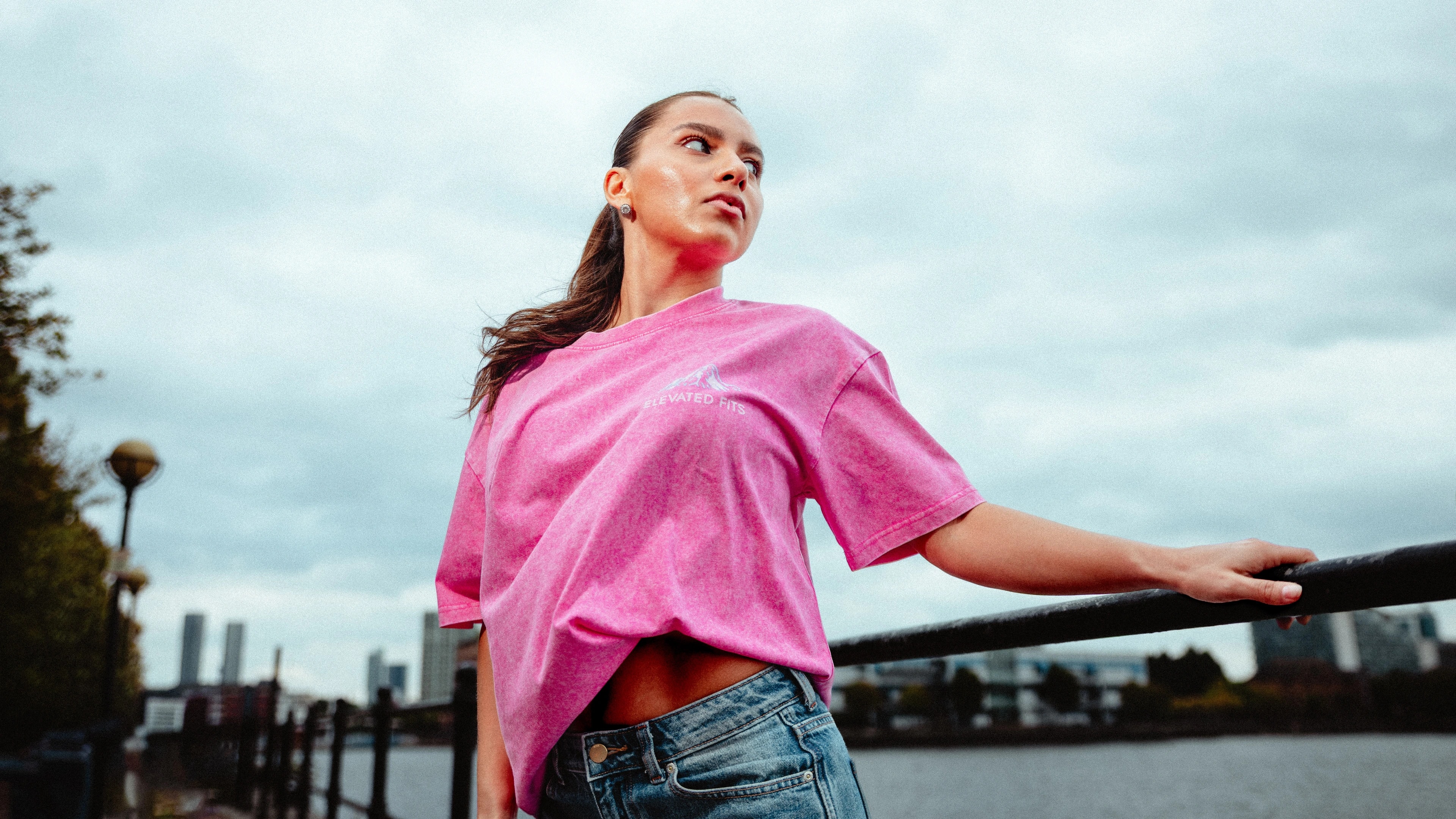 A woman wearing a pink streetwear shirt poses beside a UK waterfront