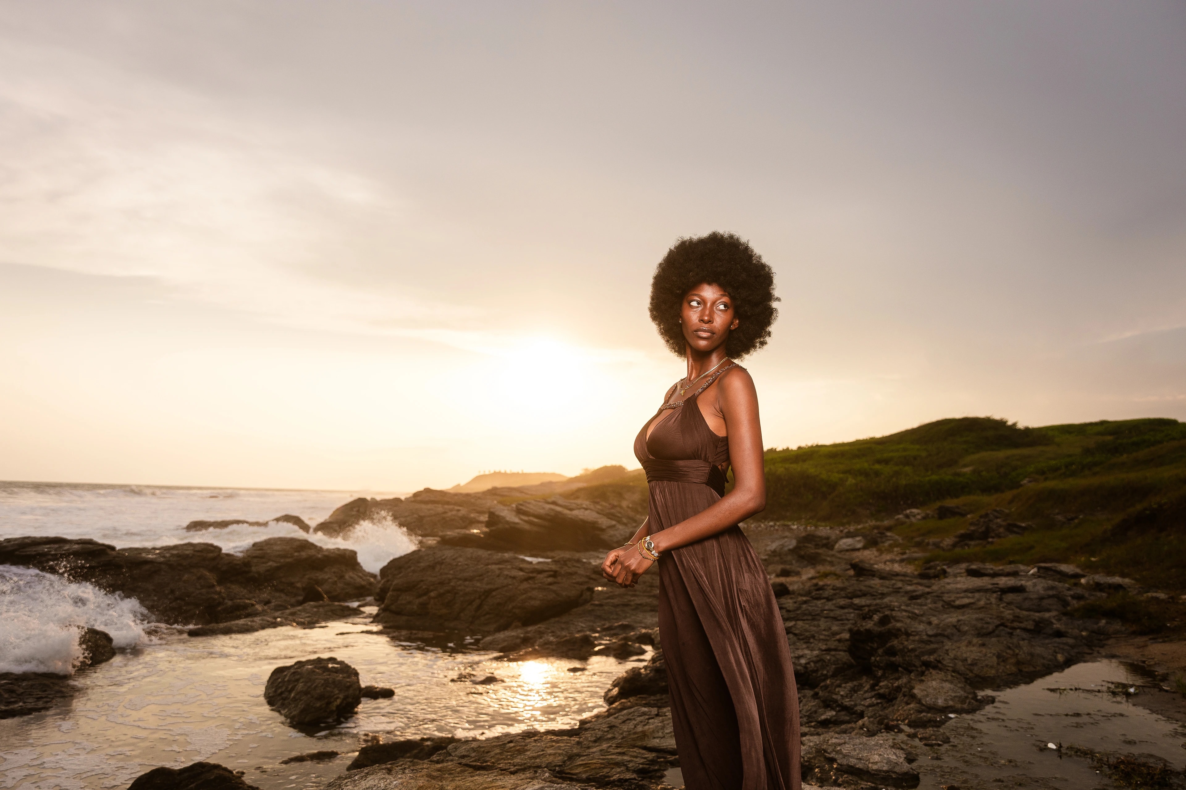 A woman stands beside the ocean in warm evening light in Ghana